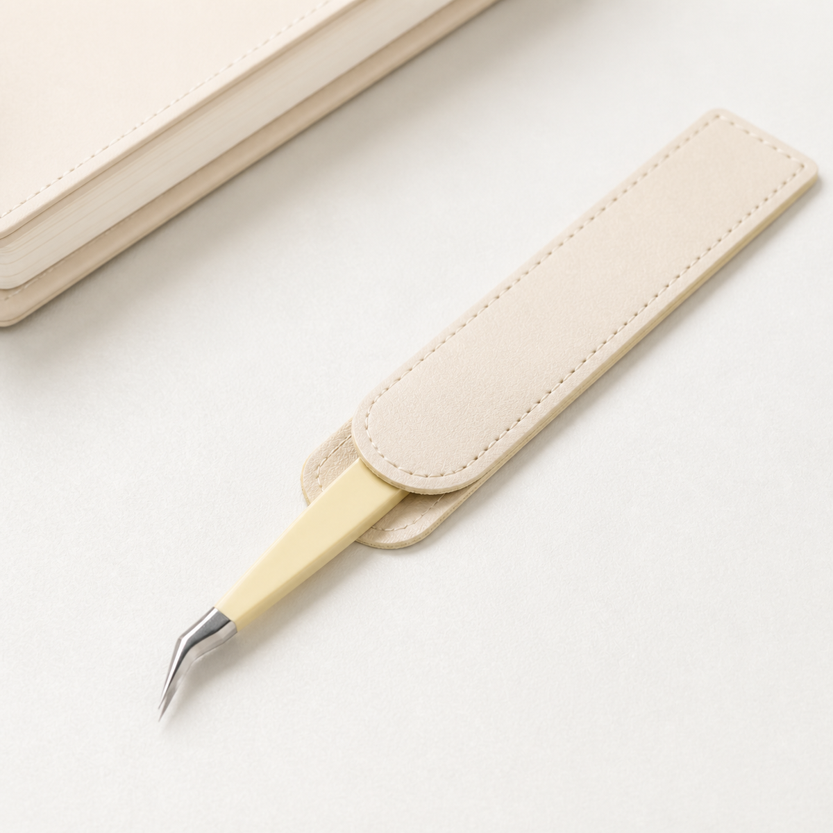 Cream angled-tip sticker tweezers partially stored in the included ivory protective case