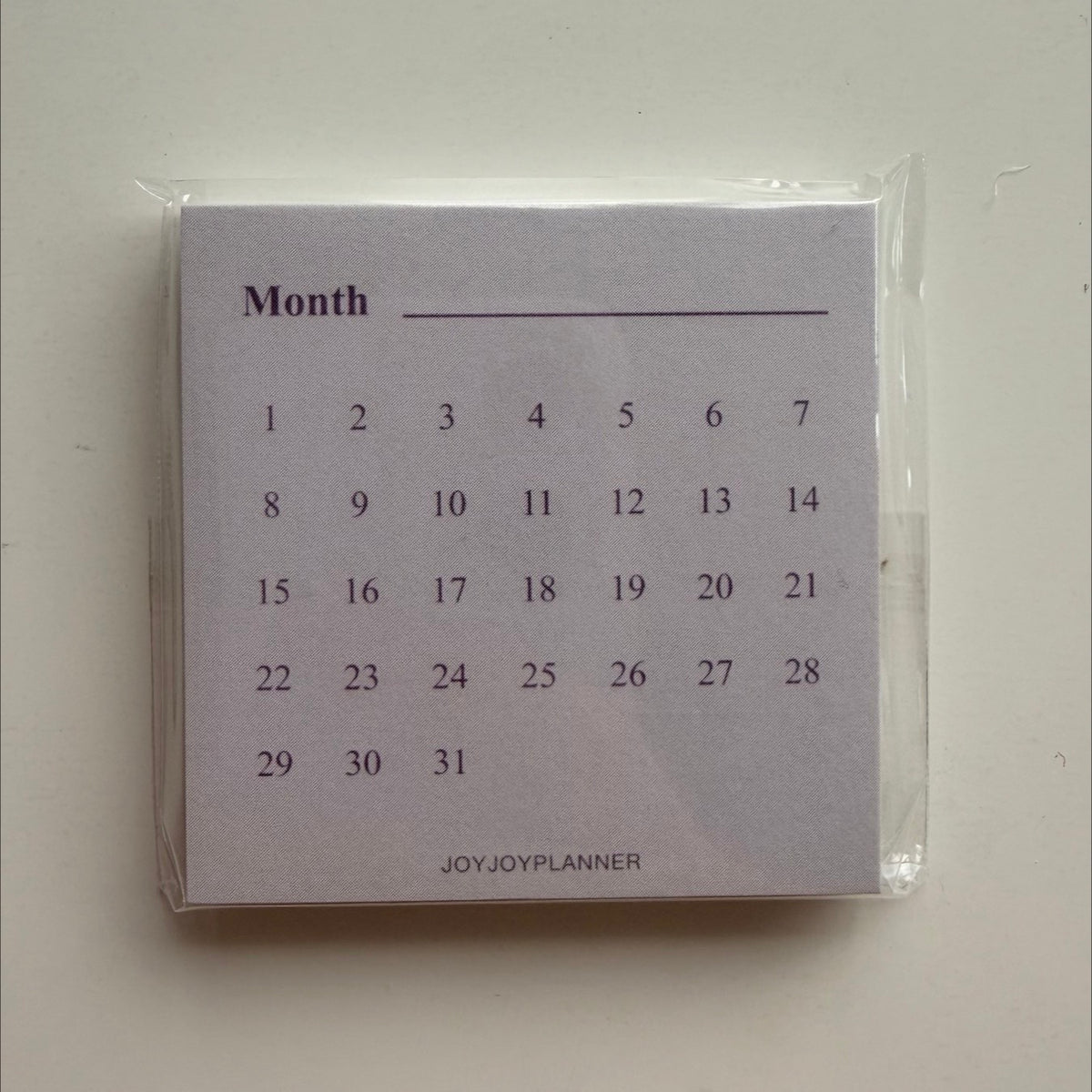 Real photo of the packaged Monthly Tracker mini memo pad with an undated 1–31 layout