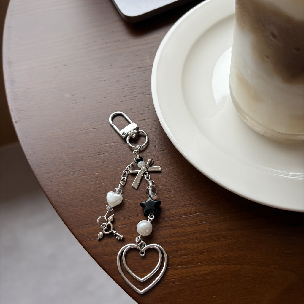 Dark double heart keychain charm with pearl details on a cafe table
