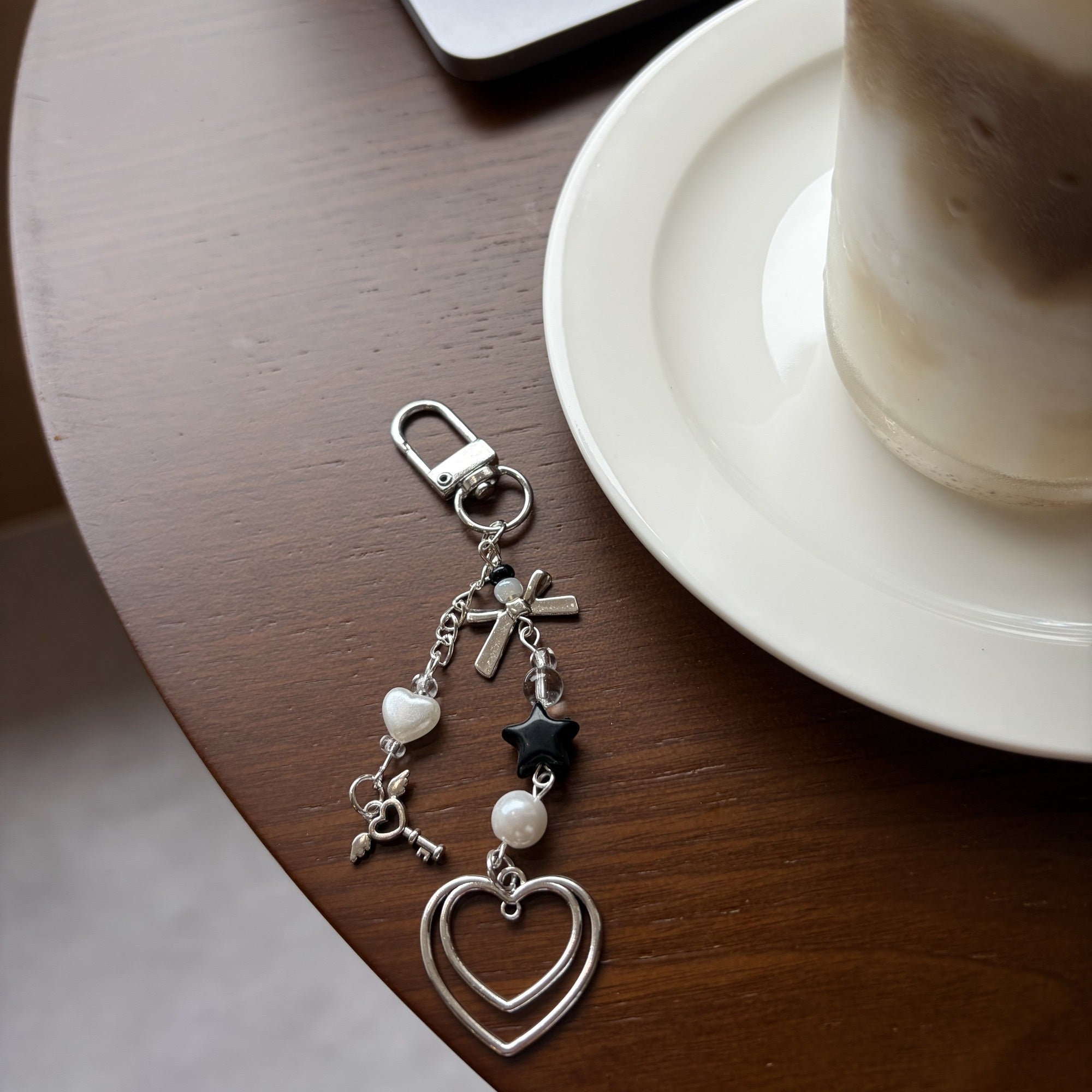 Dark double heart keychain charm with pearl details on a cafe table