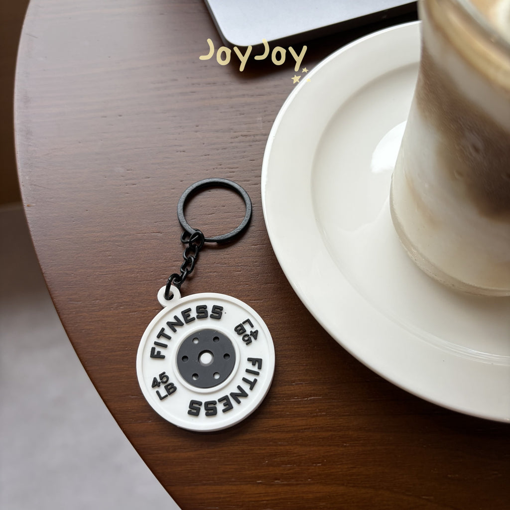 White gym weight plate planner charm with black lettering styled on a cafe table